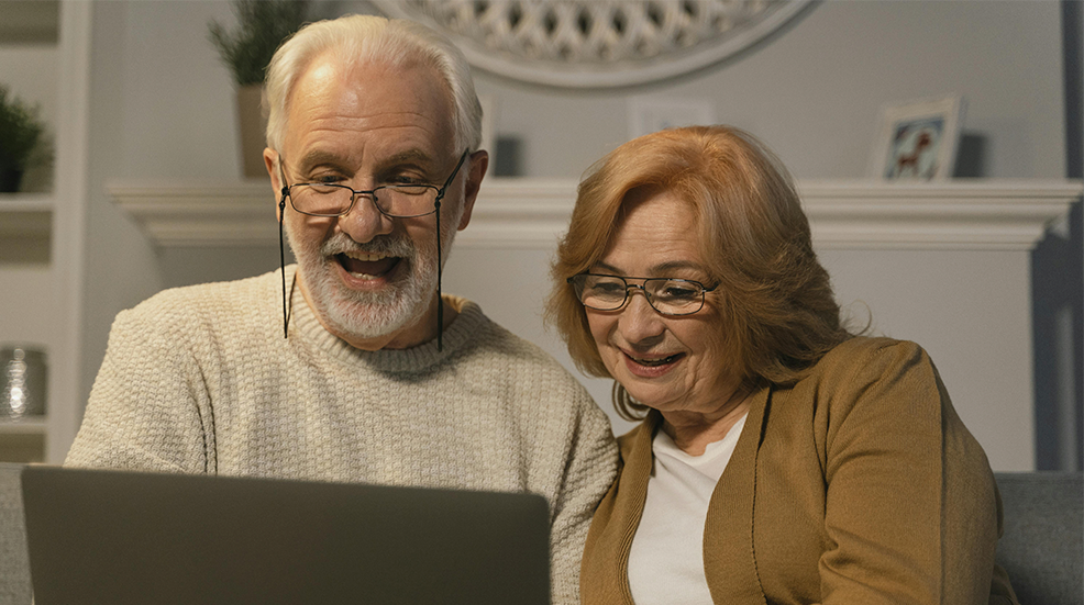 An older couple using a laptop together and looking cheery